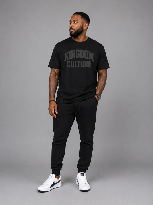 Man wearing a black 'Kingdom Culture' t-shirt and black pants on a gray background