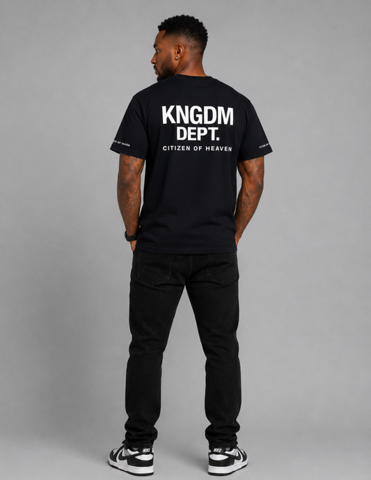 Person wearing a black t-shirt with 'KNGM DEPT.' text on the back against a gray background