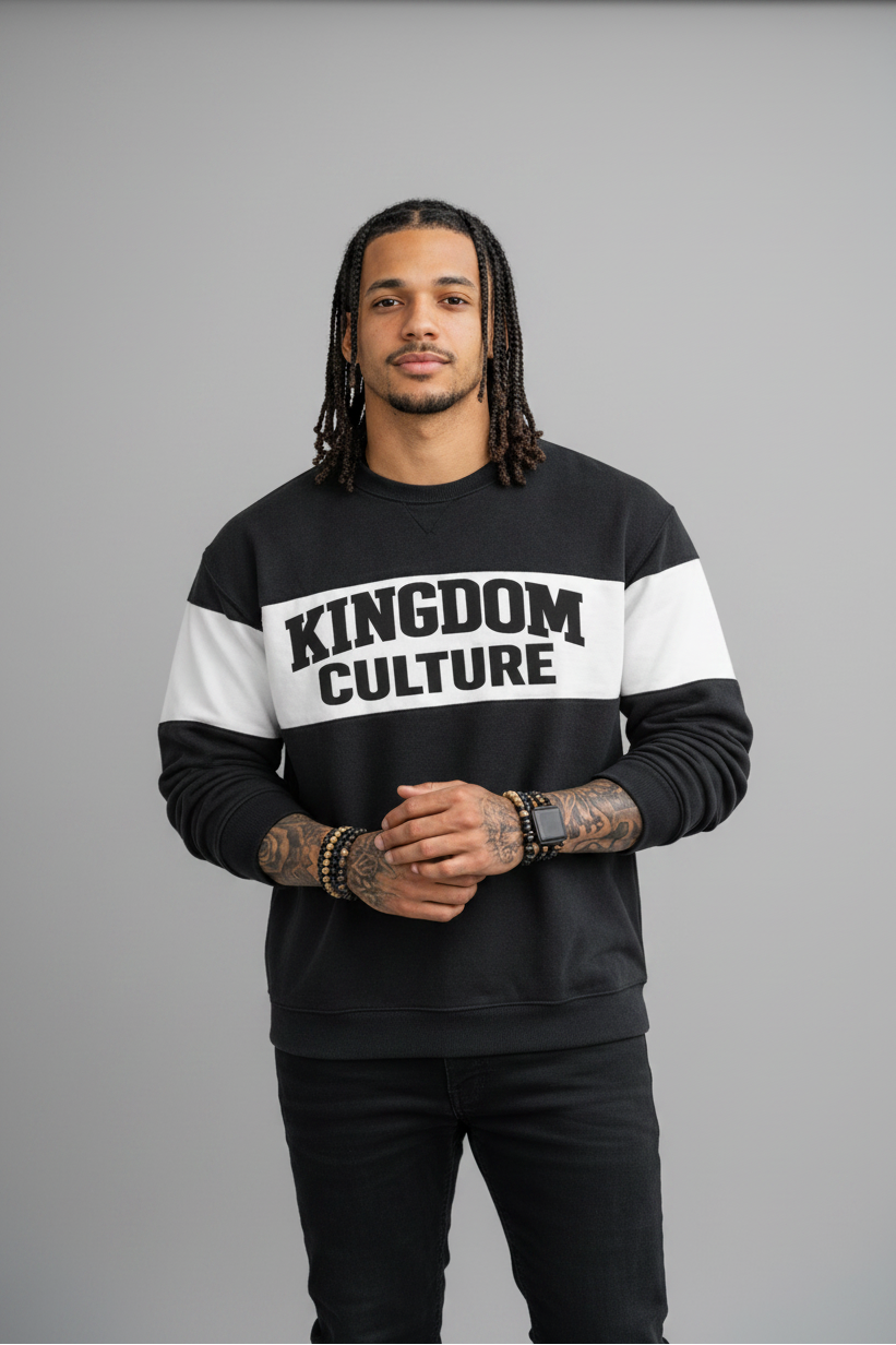 Person wearing a black and white 'Kingdom Culture' sweatshirt leaning against a brick wall.