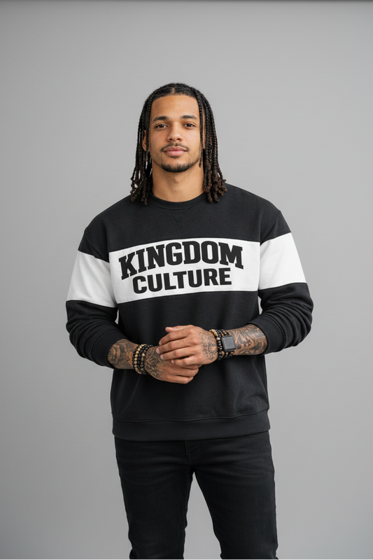 Person wearing a black and white 'Kingdom Culture' sweatshirt leaning against a brick wall.