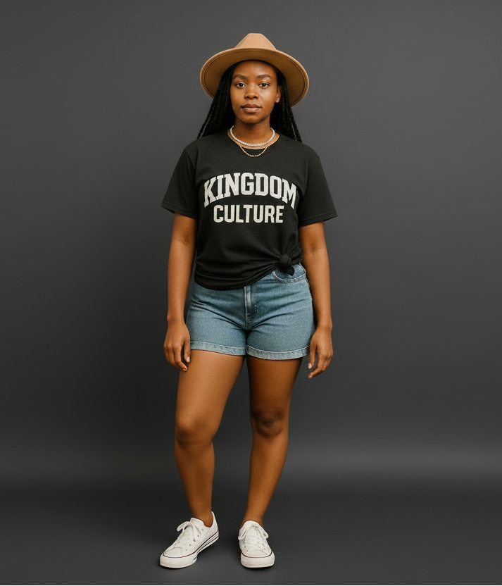 Person wearing a black 'Kingdom Culture' t-shirt, denim shorts, and a hat on a beige background